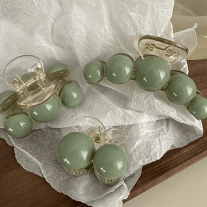 Sage green pearl claw clips and cherry hair pins set on a wooden tray for styling