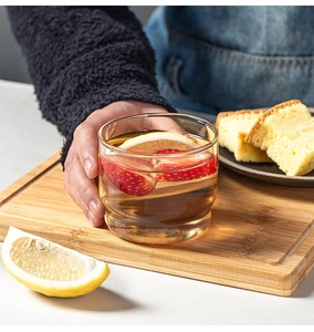 Detail of hand holding a heat-resistant glass cup with fruit slices on wood board