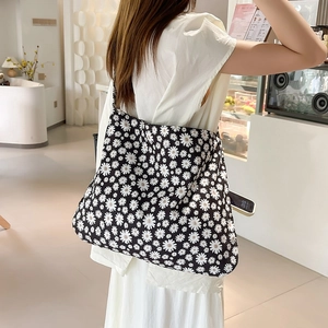 Spacious black canvas shoulder bag with white daisy floral print worn in a cafe setting