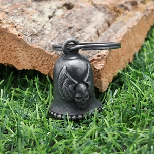 Macro shot of a vintage silver skull bell pendant with wings on natural bark texture