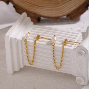 Minimalist gold stainless steel earrings with freshwater pearls and tassels on white podium