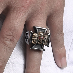 Detail of cross-shaped steel ring with three skulls and red gemstone eyes