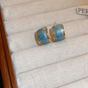 Detail view of gold C-shape stud earrings with marble sky blue enamel on a jewelry box
