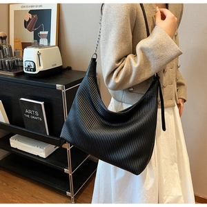 Détail du sac Hobo noir plissé avec bandoulière chaîne porté par un mannequin en intérieur