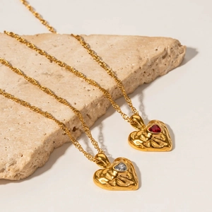 Golden heart pendant necklaces with textured surface and crystals on a stone display