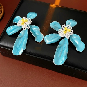 Détail macro de boucles d'oreilles fleurs en émail bleu avec centre perlé sur cuir