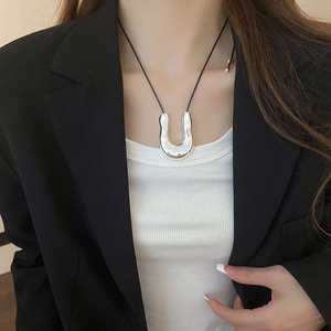 Macro view of polished silver U-shape pendant on a black slim cord necklace