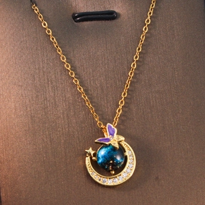 Detail of crescent moon pendant with blue galaxy orb and purple butterfly on gold chain