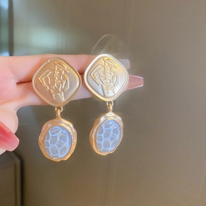 Close-up of vintage gold earrings with abstract face relief and blue faux stone pendant