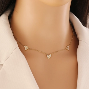 Gros plan d'un collier doré avec cœurs en émail blanc porté par un mannequin en veste beige