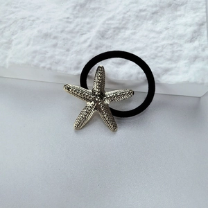 Macro detail of textured golden starfish ornament on a high-elastic black hair tie