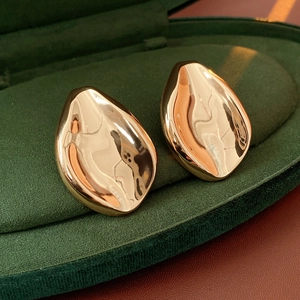 Macro shot of polished gold irregular teardrop earrings on green velvet jewelry box