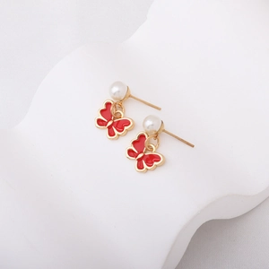 Détail de boucles d'oreilles papillon rouge avec bordure dorée et perles blanches