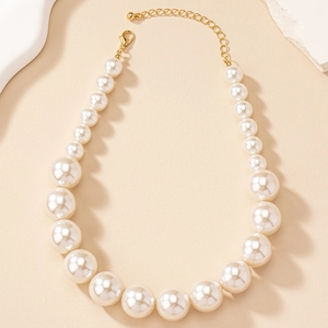 Graduated white faux pearl necklace with gold lobster clasp on warm sandy background