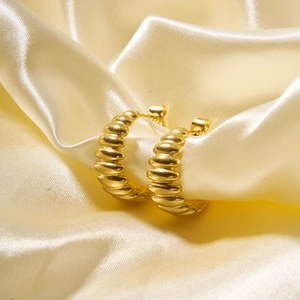 Macro shot of gold croissant hoop earrings with a twisted texture on silk fabric