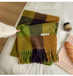 Close-up of green and brown plaid scarf texture with tassels and Superwoman label
