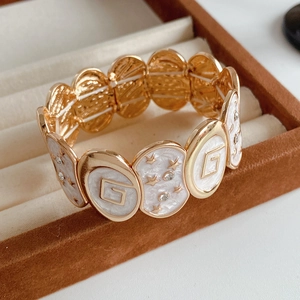 Détail d'un bracelet vintage en or avec émail blanc, motifs d'étoiles et relief lettre G
