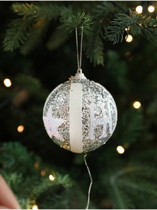 Close-up of a silver glitter Christmas ball with star patterns on a festive pine tree