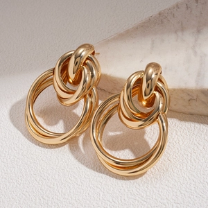 Detail of gold knot earrings with polished metal rings on a minimalist textured stone