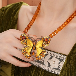 Macro detail of vintage butterfly pendant with amber stones and beaded sweater chain