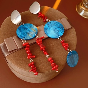 Close-up of asymmetrical earrings with blue resin stones and red coral-style beads
