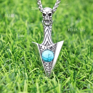 Macro view of gothic skull arrowhead pendant with turquoise stone and chain on grass