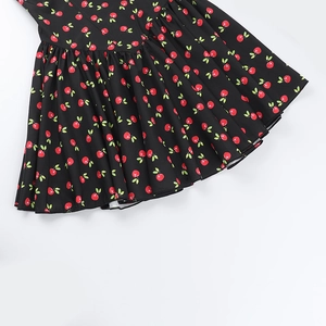 Detail of summer dress featuring red cherry print and pleated black fabric texture
