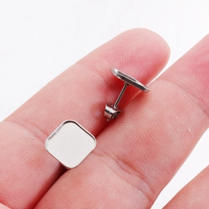Pair of square and round silver stainless steel earring stud bases on a fingertip