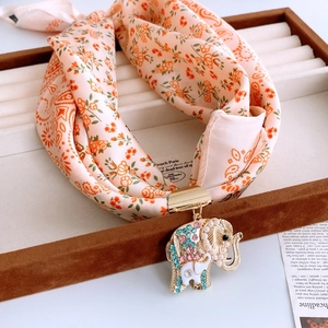 Détail du pendentif éléphant doré avec cristaux sur foulard en soie à fleurs orange