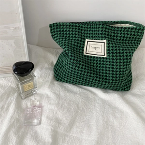 Close-up of green and black houndstooth toiletry bag on white fabric with perfume bottle