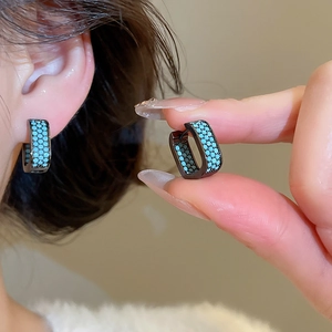 Close-up of black geometric hoop earrings with turquoise blue cubic zirconia stones