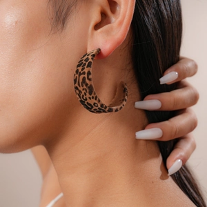 Close-up of a model wearing large leopard print velvet C-shaped hoop earrings