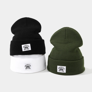 Three Brooklyn knitted beanies in black, white, and green with a street style patch