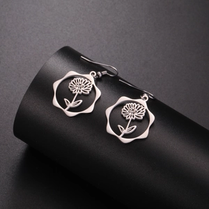 Detail view of silver stainless steel daisy drop earrings on a black display stand