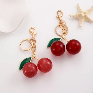 Detail of red glitter cherry keychains with golden metal clasp on a white tray