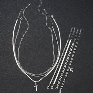 Flat lay of minimalist silver cross pendant necklace and multilayer chain bracelets set