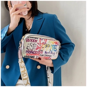 Detail of colorful graffiti crossbody camera bag with wide patterned strap on blue blazer