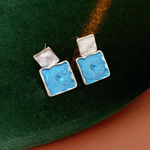 Detail of square blue and white enamel earrings with gold frames on green velvet