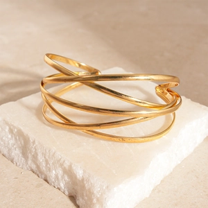 Detail view of a gold multi-layer crossover open cuff bracelet on a stone base
