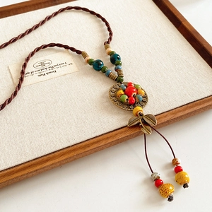 Macro detail of ethnic ceramic beaded necklace with leaf pendant on rustic wooden tray