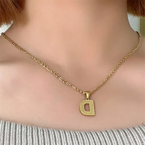 Dettaglio di una collana a catena Figaro dorata con ciondolo a lettera D su una modella
