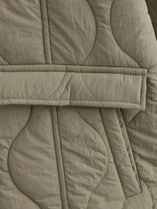 Detailed macro view of olive green quilted jacket featuring wavy patterns and pocket flap
