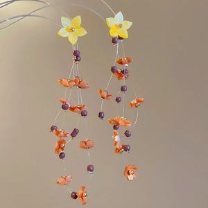 Detail of yellow resin flower earrings with pink petals and colorful beaded tassels