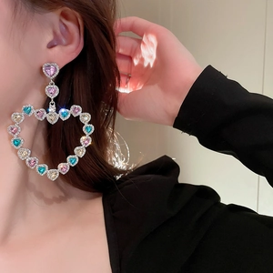 Détail macro de boucles d'oreilles cœur avec cristaux colorés portées par un mannequin