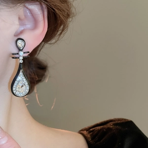 Detail eines tropfenförmigen Ohrrings mit Emaille und Zirkonen an Samtkleidung