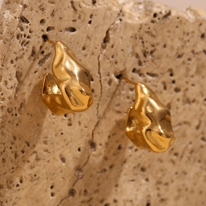 Macro shot of gold hammered metal earrings on a textured natural porous rock background