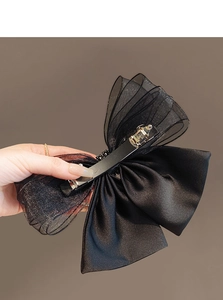 Detail of black mesh bow hair clip showing dual-layer satin fabric and metal spring clasp