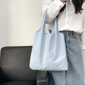 Detail of light blue polka dot canvas tote bag worn by a model in a bright room