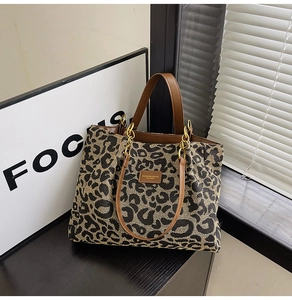 Detail view of large leopard print tote bag with brown leather handles and metal hardware