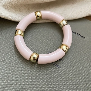 Detail view of light pink acrylic tube beads and polished gold metal rings on a bracelet